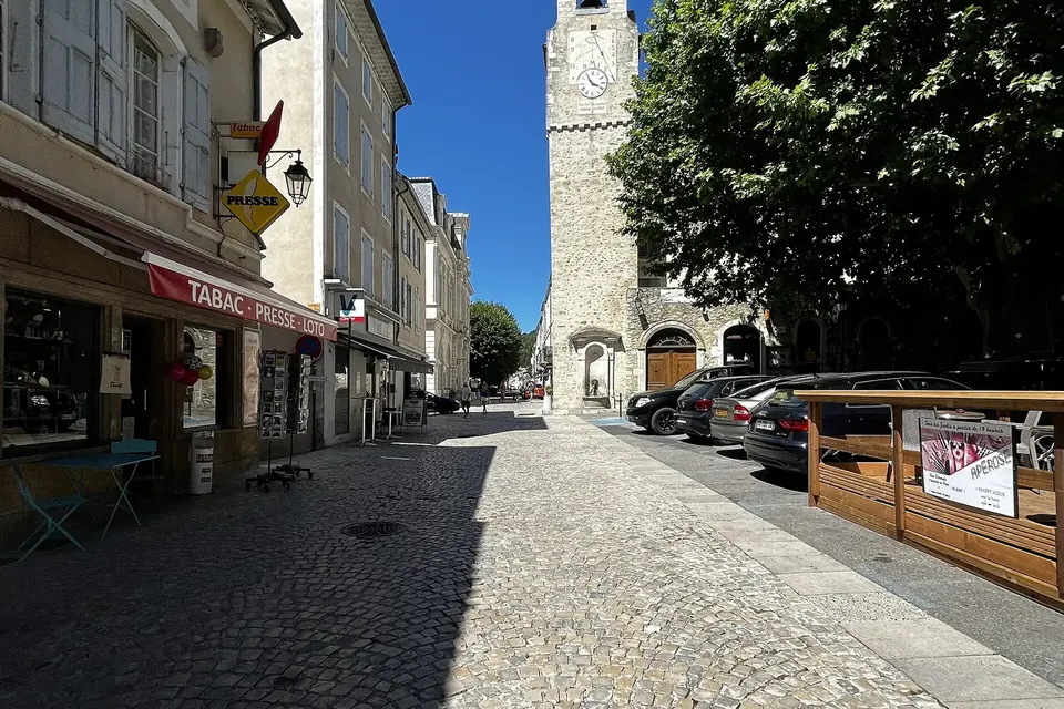 La rue du Bourg à Dieulefit, rue pavée bordée de maisons et de commerces, avec au fond la tour du beffroi