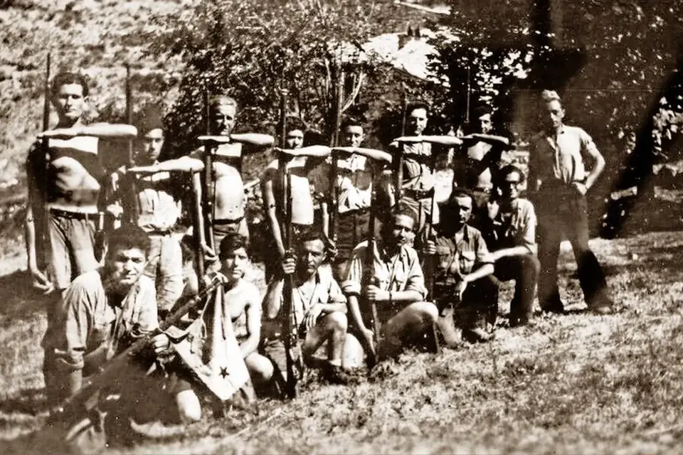 Photographie de groupe de maquisards en 1944, une vingtaine d'hommes jeunes posant debout et accroupis devant des arbres