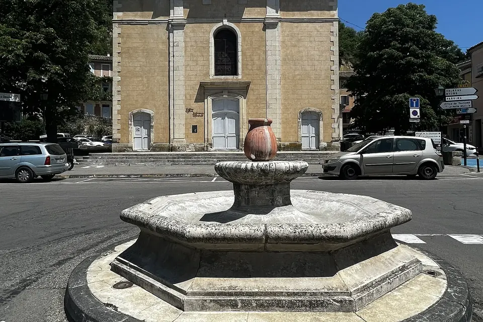 Le temple protestant de Dieulefit, façade claire à fronton, derrière une fontaine octogonale surmontée d'une poterie, place Châteauras