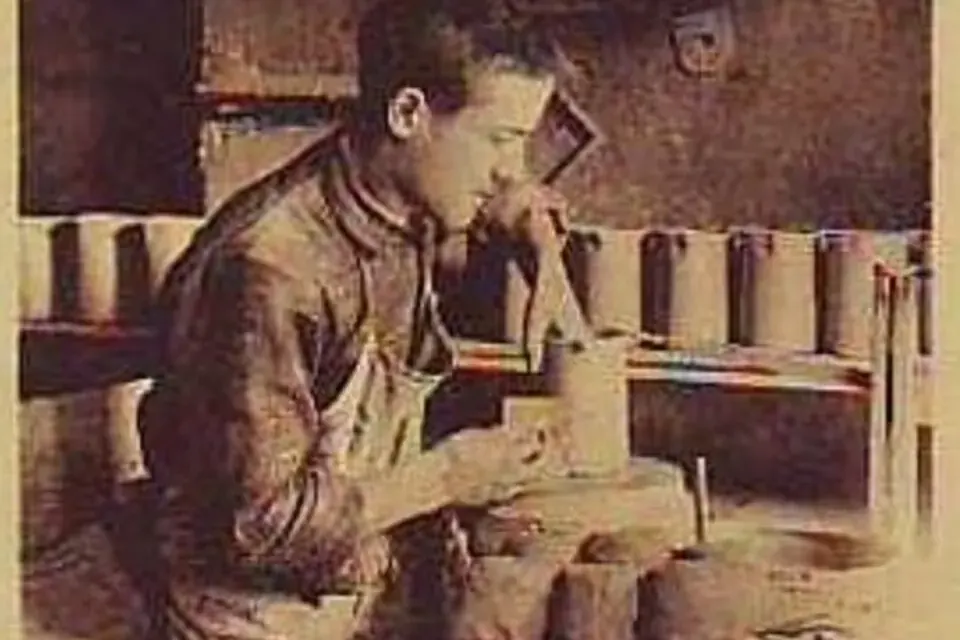 Carte postale ancienne en sépia montrant un potier de Dieulefit assis à son tour, façonnant un pot, devant des étagères chargées de pièces